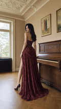 Woman wearing burgundy strapless lace evening gown with high slit, back view