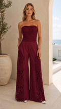 Burgundy strapless wide leg jumpsuit with textured bodice and openwork side leg panels front view