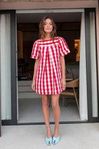 Front view of woman wearing red gingham check pleated mini dress with light blue heels