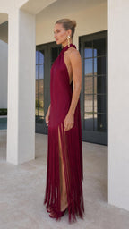 Model wearing burgundy satin halter fringe maxi dress side view
