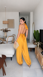 Back view of mustard backless halter jumpsuit with tie closure and flowing legs