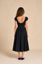 Back view of woman in black smocked midi dress against neutral background