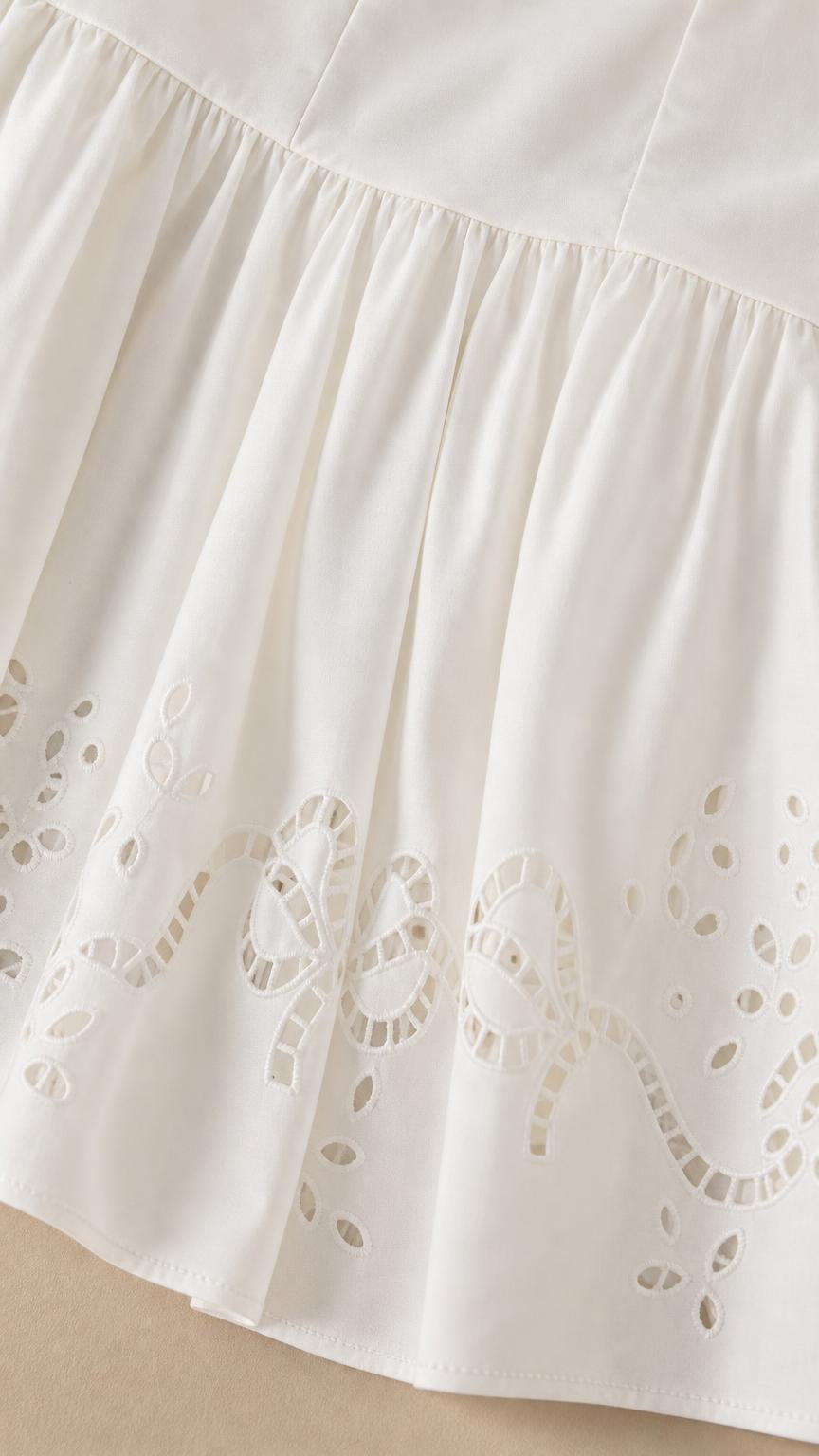 Close-up of embroidered cutwork hem on white mini dress