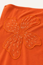 Close-up of orange fabric with floral embroidery and bead accents