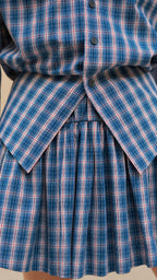 Close-up detail of blue plaid shirt button closure and pleated skirt overlay