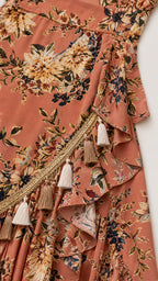 Close-up of tassel trim and ruffles on rust floral wrap dress