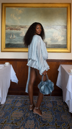 Side view of powder blue pleated long sleeve romper with ruffled shorts and flowing sash detail