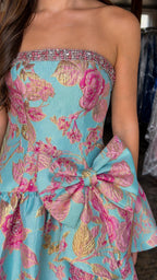 Close-up detail of crystal-trimmed neckline and waist bow on blue floral dress