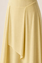 Close-up detail of pleated waist and asymmetric layered skirt on yellow dress