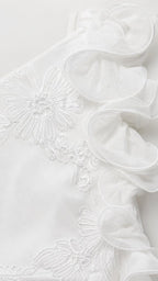Close-up detail of fabric, ruffles, and floral embroidery