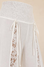 Close-up detail of the lace waistband and side ties on the white trousers