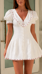Close-up of white dress showing V-neck collar, front buttons, and embroidered trim